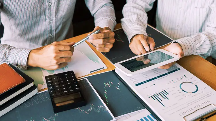 Two professionals reviewing procurement cost and performance charts on paper and a tablet