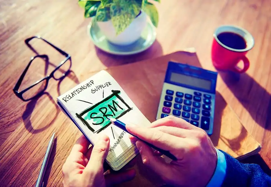 A hand writes SRM and supplier relationship management notes next to a calculator on a desk